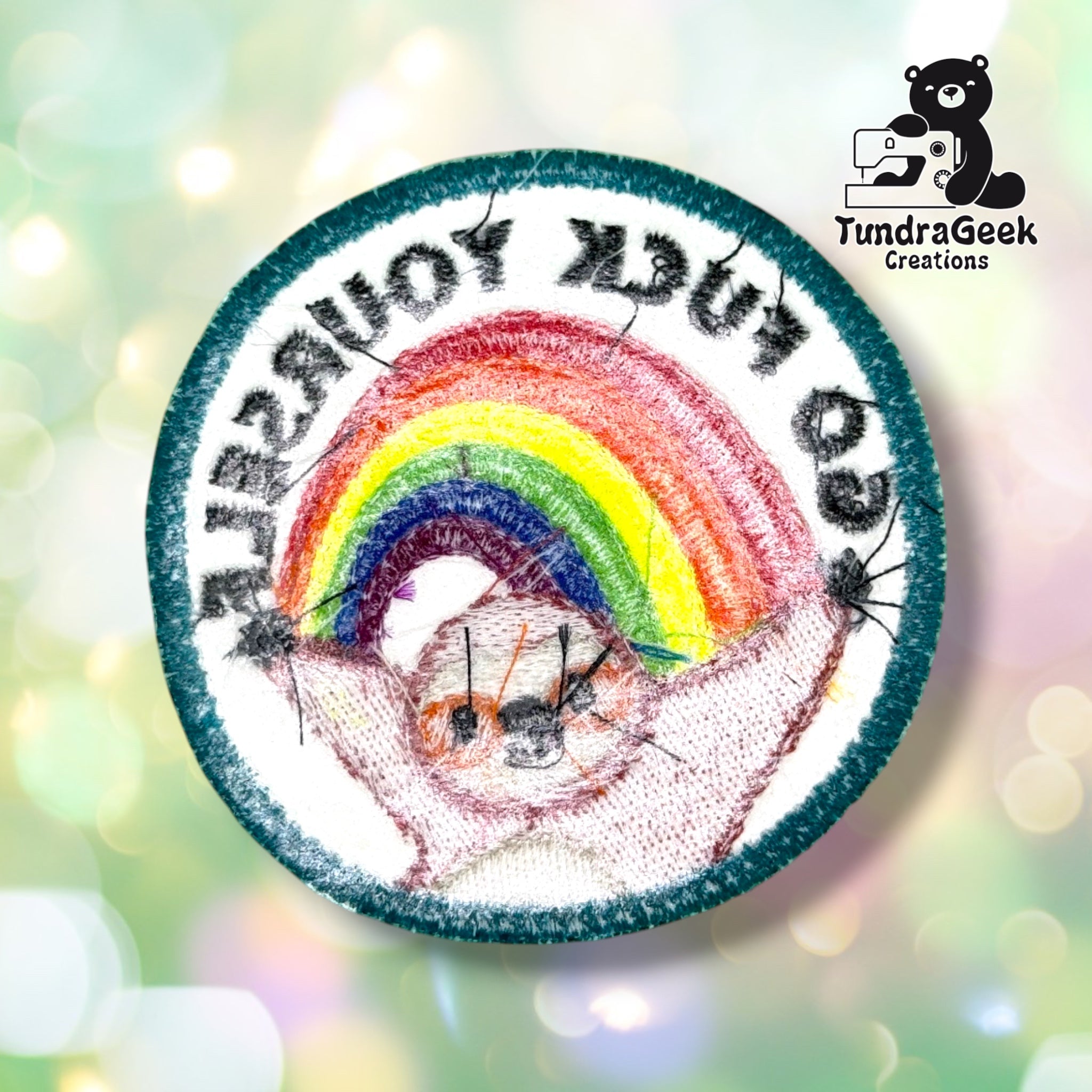 Back of the patch showing the reverse side of the embroidery in muted thread colors, with the rainbow and sloth shapes and mirrored lettering faintly visible through the white twill backing.