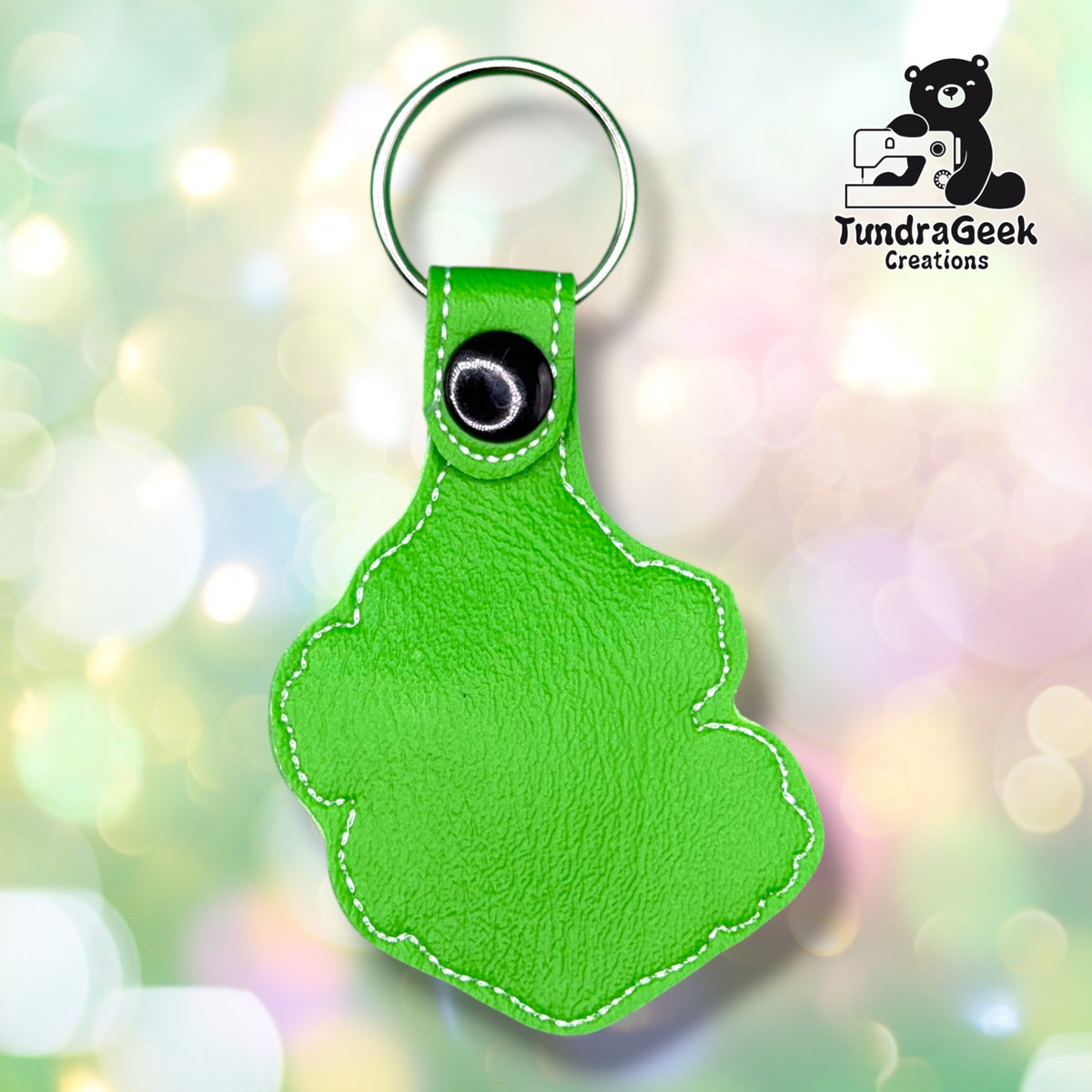 The back side of the Grinch Keychain, showing off a bright green vinyl with white stitching around the edges. There's a tab of the vinyl that goes around a split ring keyring secured with a black plastic snap.