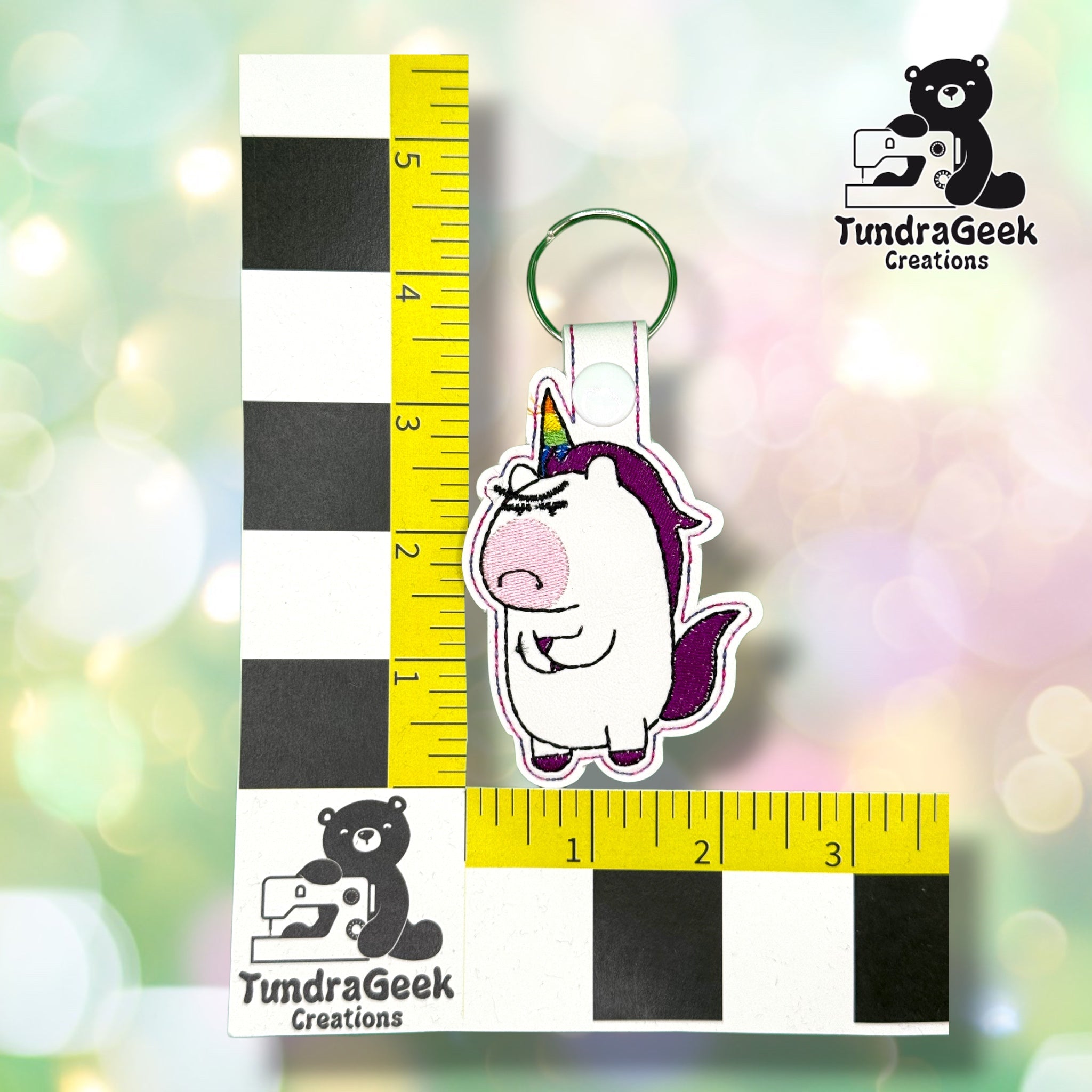 Keychain shown against a black-and-white checkered background with yellow rulers for scale, measuring approximately 4.5 inches tall by 2.5 inches wide including hardware.