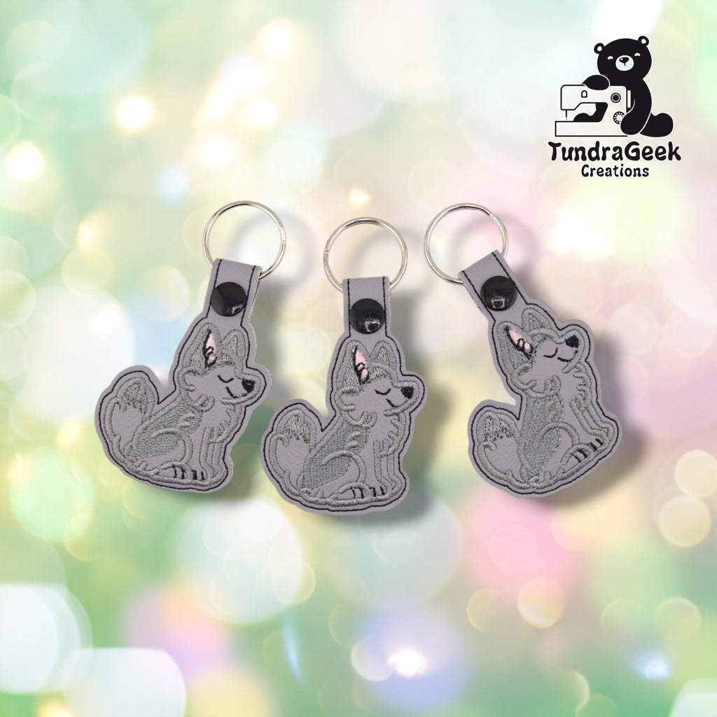 Three identical husky keychains hanging side by side at slightly different angles, each in light grey faux leather with the same darker grey stitched husky, black plastic snap and silver split ring.