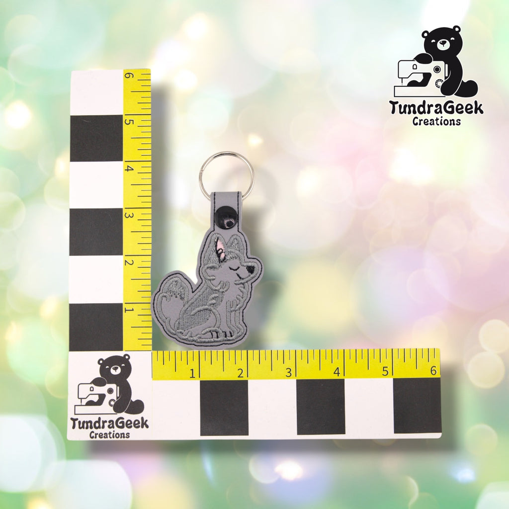 The husky keychain photographed against a yellow ruler marked in inches along both edges, for size reference. It measures 4.25 inches tall by 2.25 inches wide including hardware.  ---
