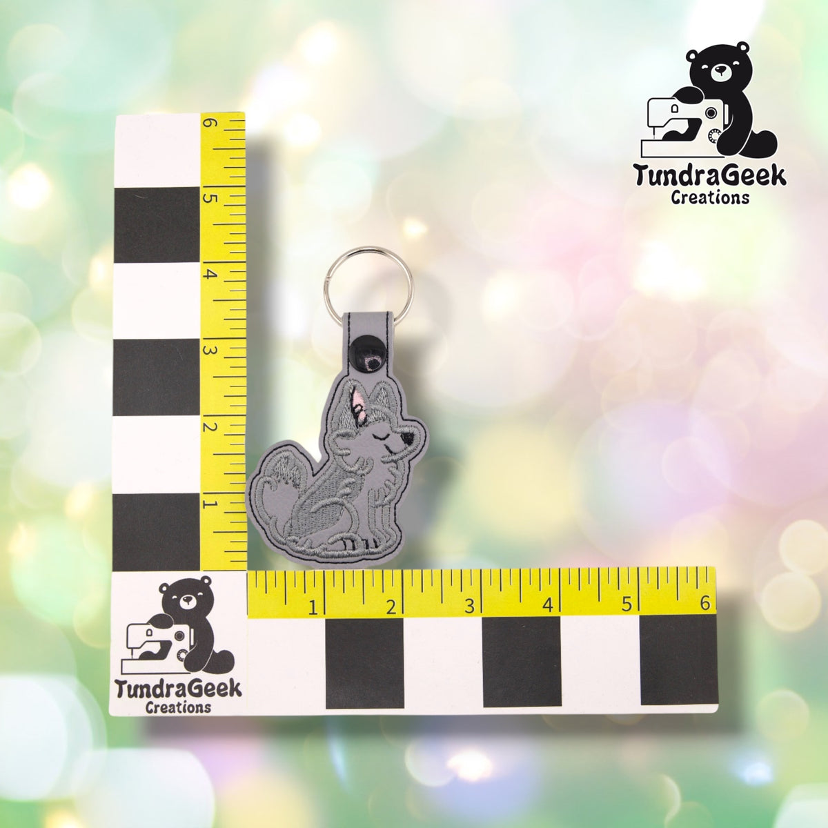 The husky keychain photographed against a yellow ruler marked in inches along both edges, for size reference. It measures 4.25 inches tall by 2.25 inches wide including hardware.  ---