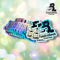 A fan of small die-cut stickers featuring a black cartoon bear holding a sewing machine, with the text 'TundraGeek Creations' on the stickers. The stickers have holographic, iridescent edges and are displayed against a soft, colorful bokeh background.