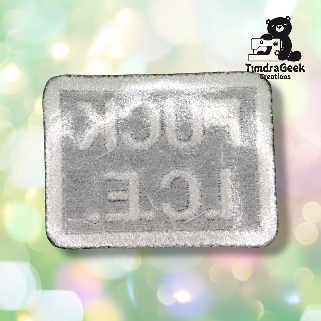 A white rectangular embroidered patch with the reversed text FUCK ICE, displayed on a blurred light background with a TundraGeek Creations bear logo in the top right corner.
