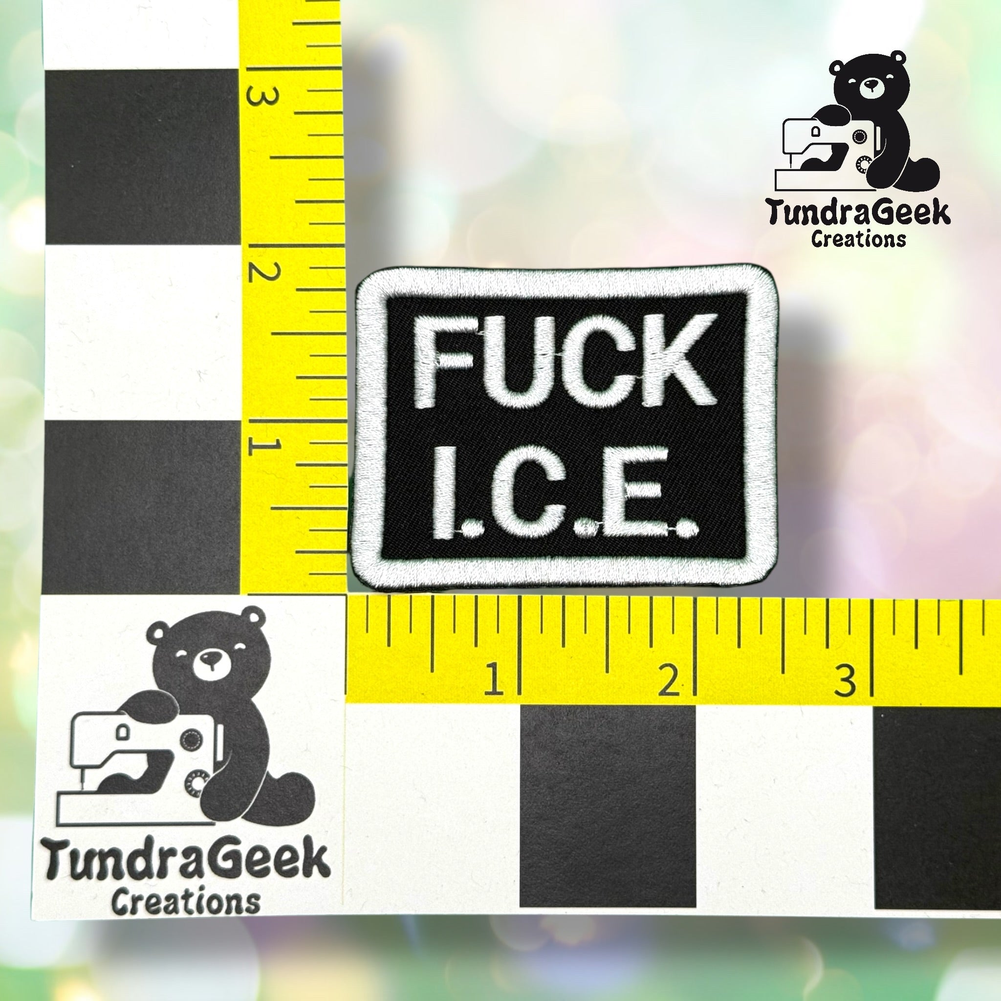 A rectangular patch with white text FUCK I.C.E. on a black background, placed on a measurement grid branded with the TundraGeek Creations logo.