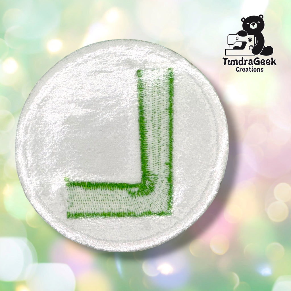 Back side of the Luigi L patch showing the iron-on adhesive for the sew-on variant. White 3in circle with a backwards L in green.