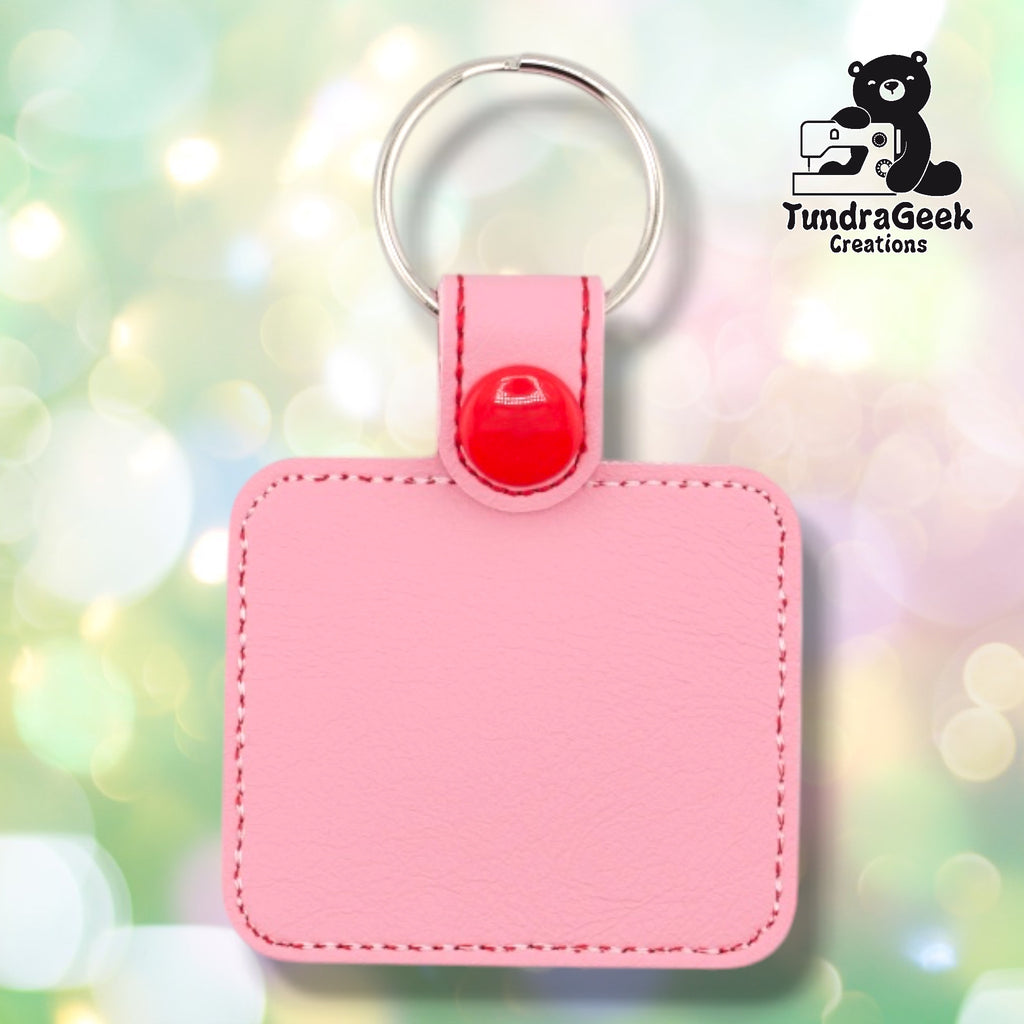 Back of a pink faux leather sewing keychain. The plain pink vinyl back panel shows red perimeter stitching on the rounded square shape. A red 12.5mm plastic snap closure secures the tab, with a silver split ring attached above.