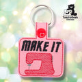 ront of a pink faux leather sewing keychain. Bold black embroidered text reading "MAKE IT" sits above an embroidered red sewing machine on a pink vinyl base with red perimeter stitching. A red 12.5mm plastic snap closure is visible on the tab, with a silver split ring above.