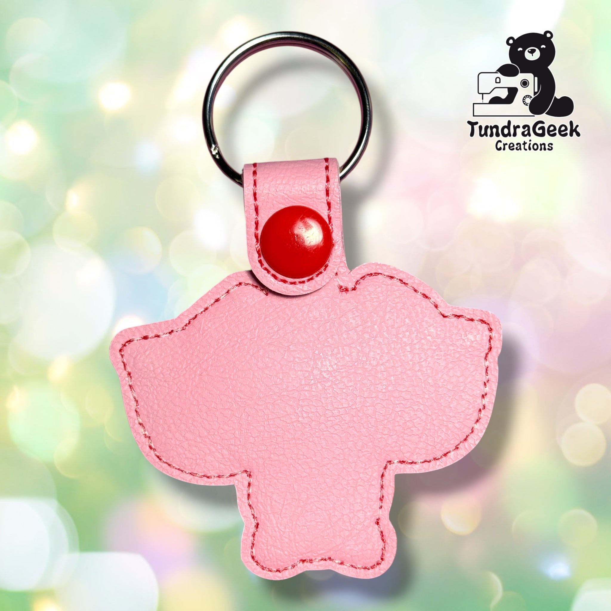 Back view of the keychain showing the plain pink vinyl backing with pink stitched edge detailing, a red plastic snap closure tab, and a silver split ring. No embroidery visible from this side.