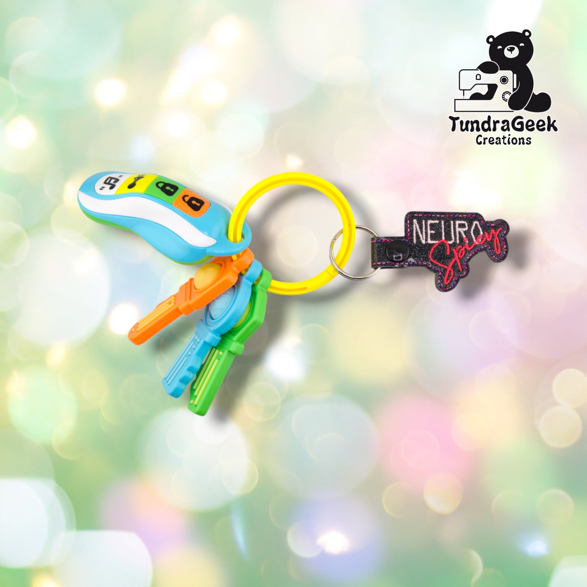The keychain clipped to a yellow silicone bangle keyring alongside a set of colorful plastic toy keys, showing it in everyday use.