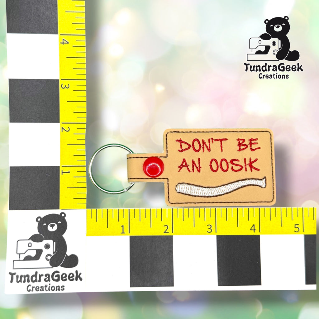 Keychain shown against a black-and-white checkered background with yellow rulers for scale, measuring approximately 4.5 inches tall by 2 inches wide including hardware.