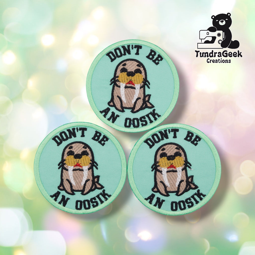 Three round embroidered patches arranged together on a soft pastel bokeh background. Each patch is mint green with a cartoon walrus, dark eyes, white tusks, and a red mouth, with "DON'T BE" arched across the top and "AN OOSIK" arched across the bottom in bold black lettering.