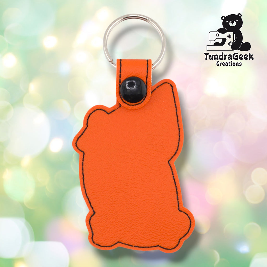 Plain back of the orange cat keychain showing orange faux leather, black outline stitching following the cat silhouette, and black snap closure. No embroidery on reverse.