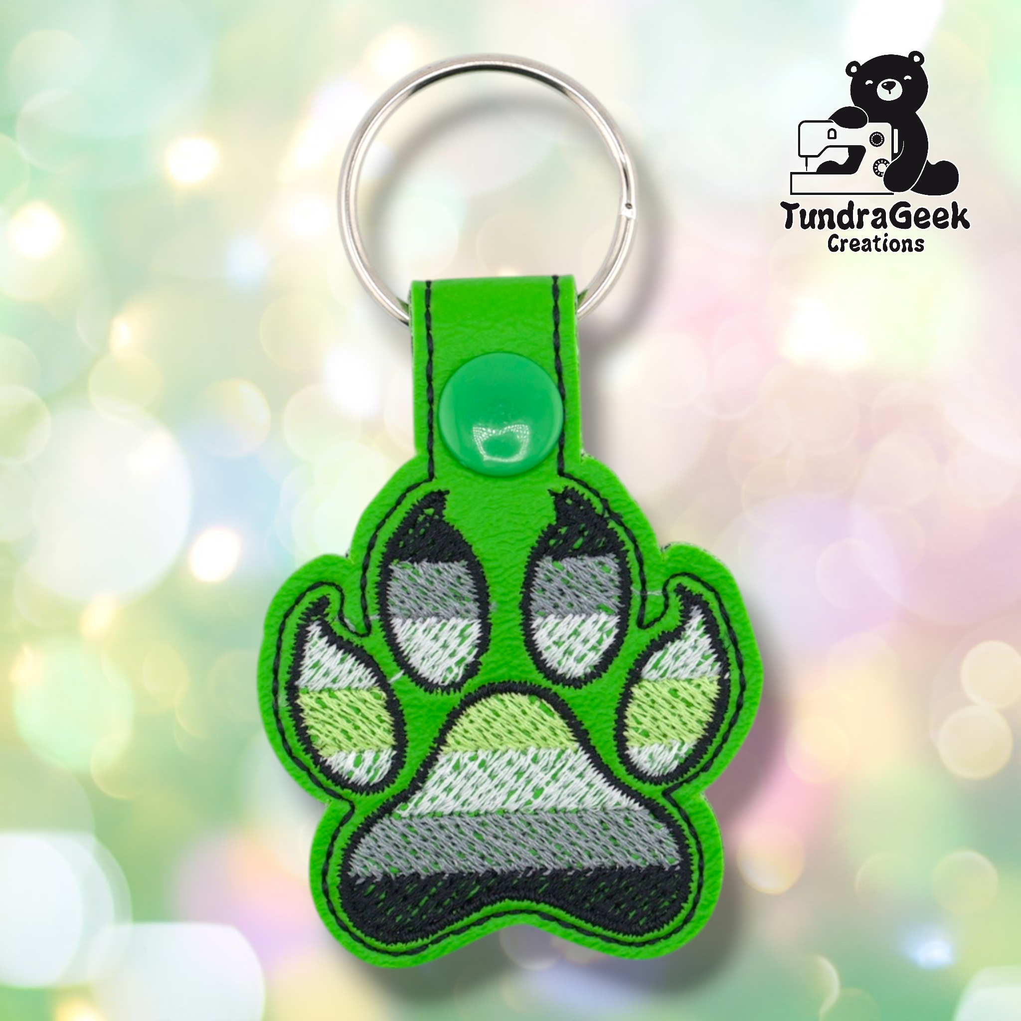 Bright green embroidered vinyl paw-shaped keychain featuring agender pride flag colors — horizontal stripes of black, gray, white, and green. The paw uses a canine-style design with clawed toe details outlined in black and bright green. Green vinyl snap tab and silver split ring hardware at top.