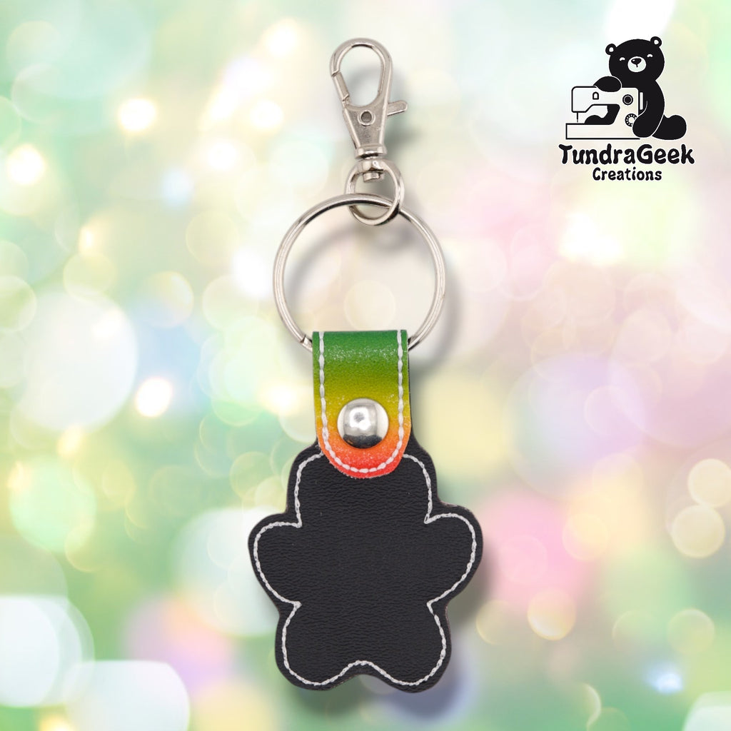 The back of the Rainbow colorway paw print keychain, showing the plain black vinyl backing with a green-to-orange ombre tab and metal rivet closure visible at the top.