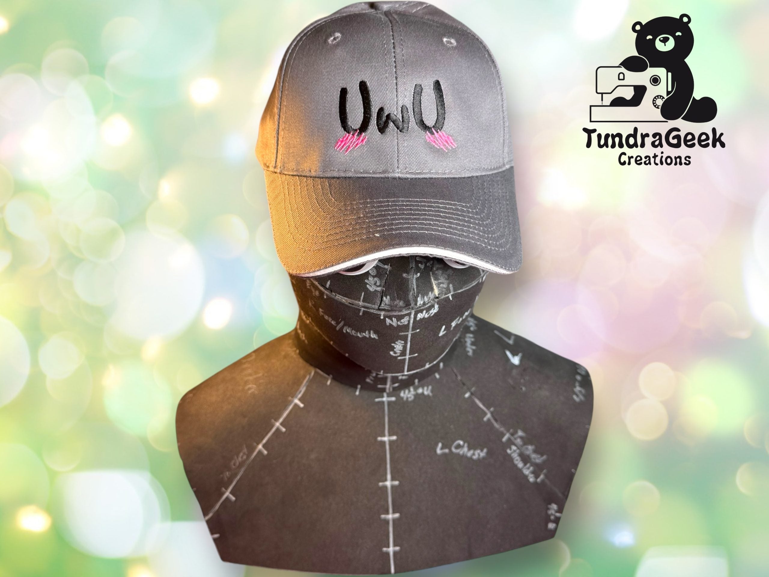 A gray baseball cap with UWU and pink whisker-like marks is displayed on a mannequin head. The TundraGeek Creations logo appears in the upper right corner.