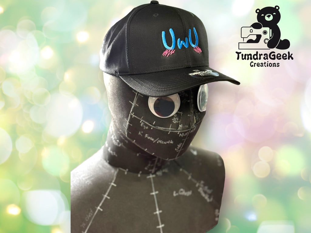 A mannequin head wearing a black hat embroidered with UWU and pink marks, with the TundraGeek Creations logo in the background.