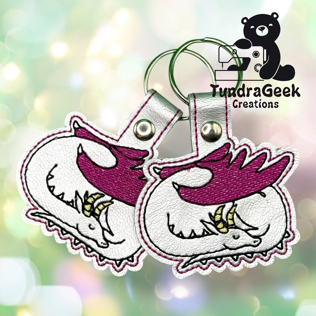Two embroidered keychains featuring a sleeping unicorn with a white body and purple mane, displayed with a TundraGeek Creations logo in the corner.