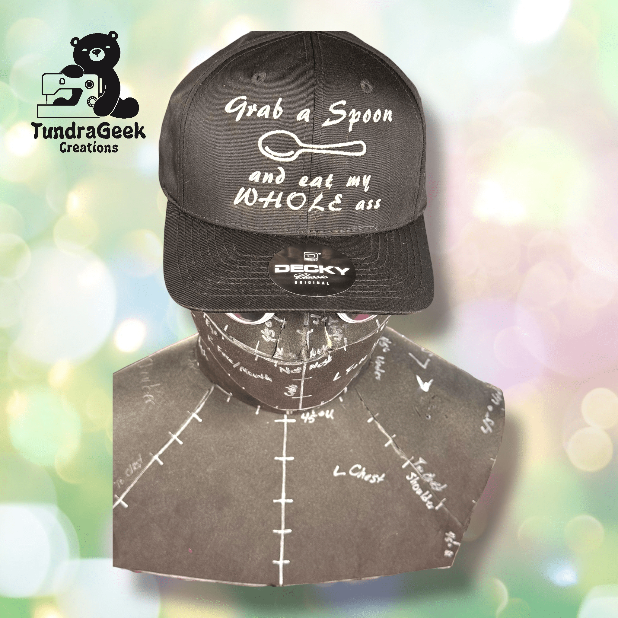 A black baseball cap with the phrase Grab a spoon and eat my whole ass displayed on a mannequin head, with a sewing logo in the top left corner.
