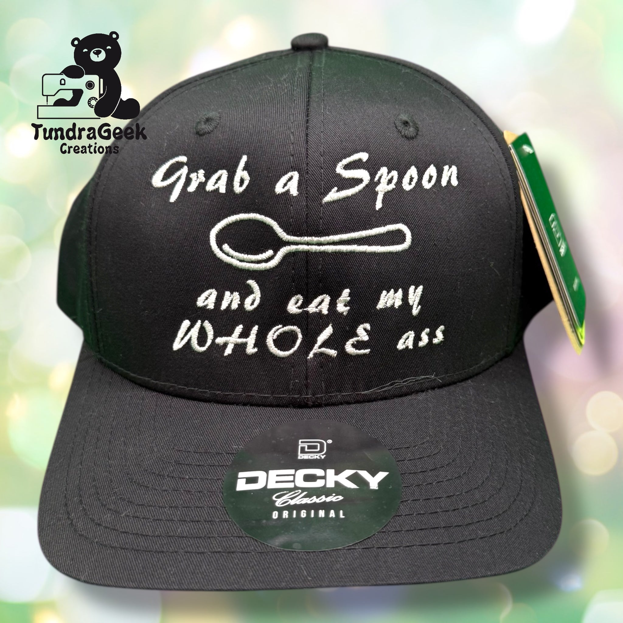 A black baseball cap with white embroidered text reading Grab a Spoon and eat my WHOLE ass and an image of a spoon above the text.