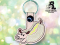 Keychain shaped like a hot dog with a dog’s face embroidered on beige fabric, attached to a metal ring. TundraGeek Creations logo appears in the upper right corner.