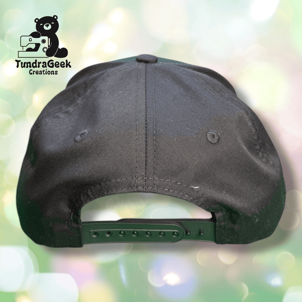 A black snapback hat viewed from the back, displayed against a blurred pastel background with the TundraGeek Creations logo in the top left corner.