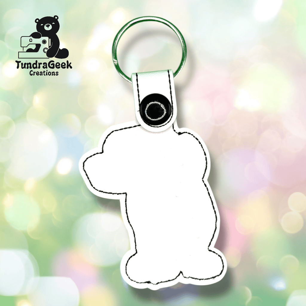White keychain in the shape of a bear with black stitching, attached to a metal keyring. Logo TundraGeek Creations with bear and sewing machine in the upper left corner.