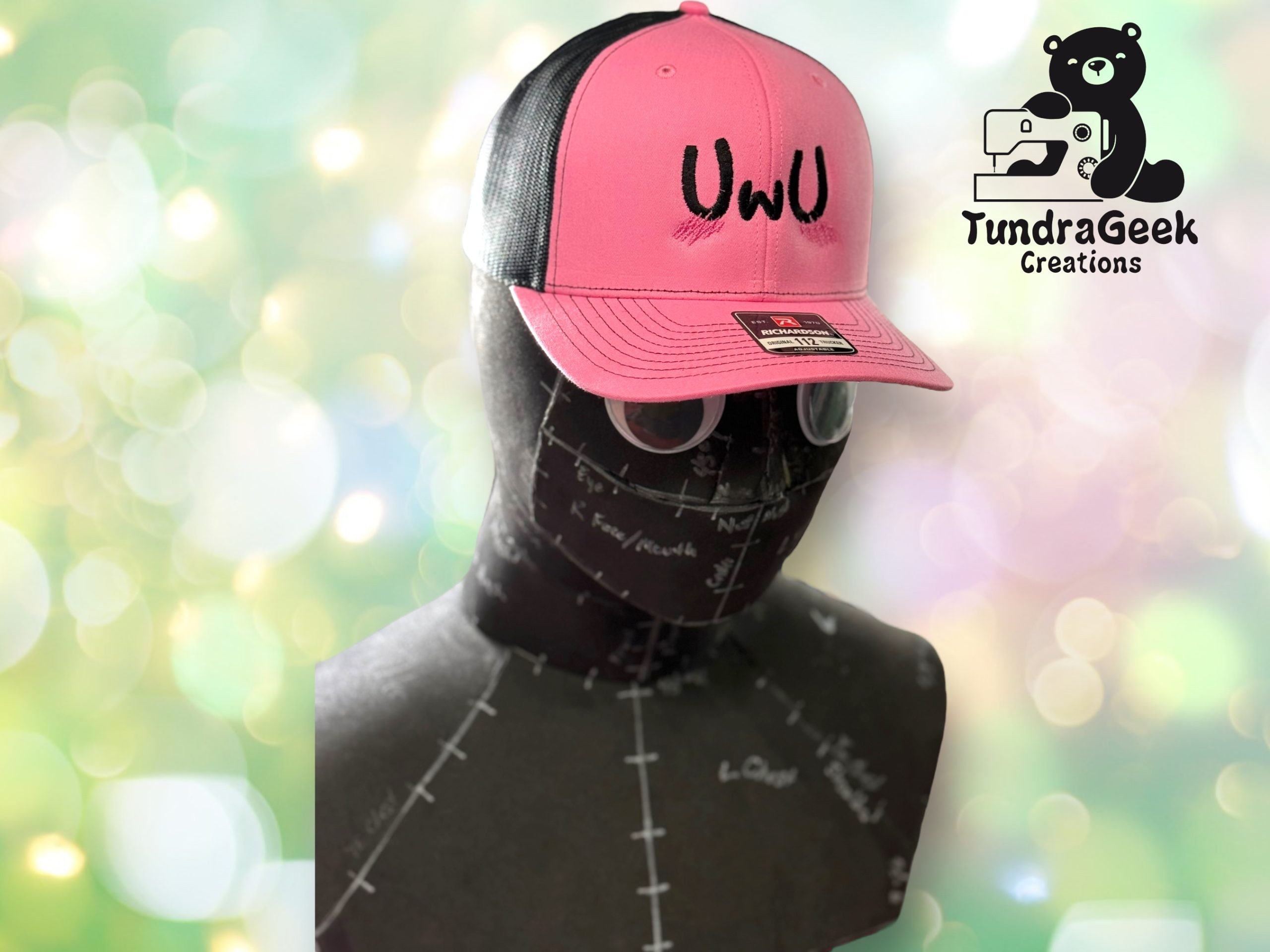A mannequin head wears a pink and black cap with UWU on the front. The TundraGeek Creations logo featuring a bear and sewing machine is in the top right corner.