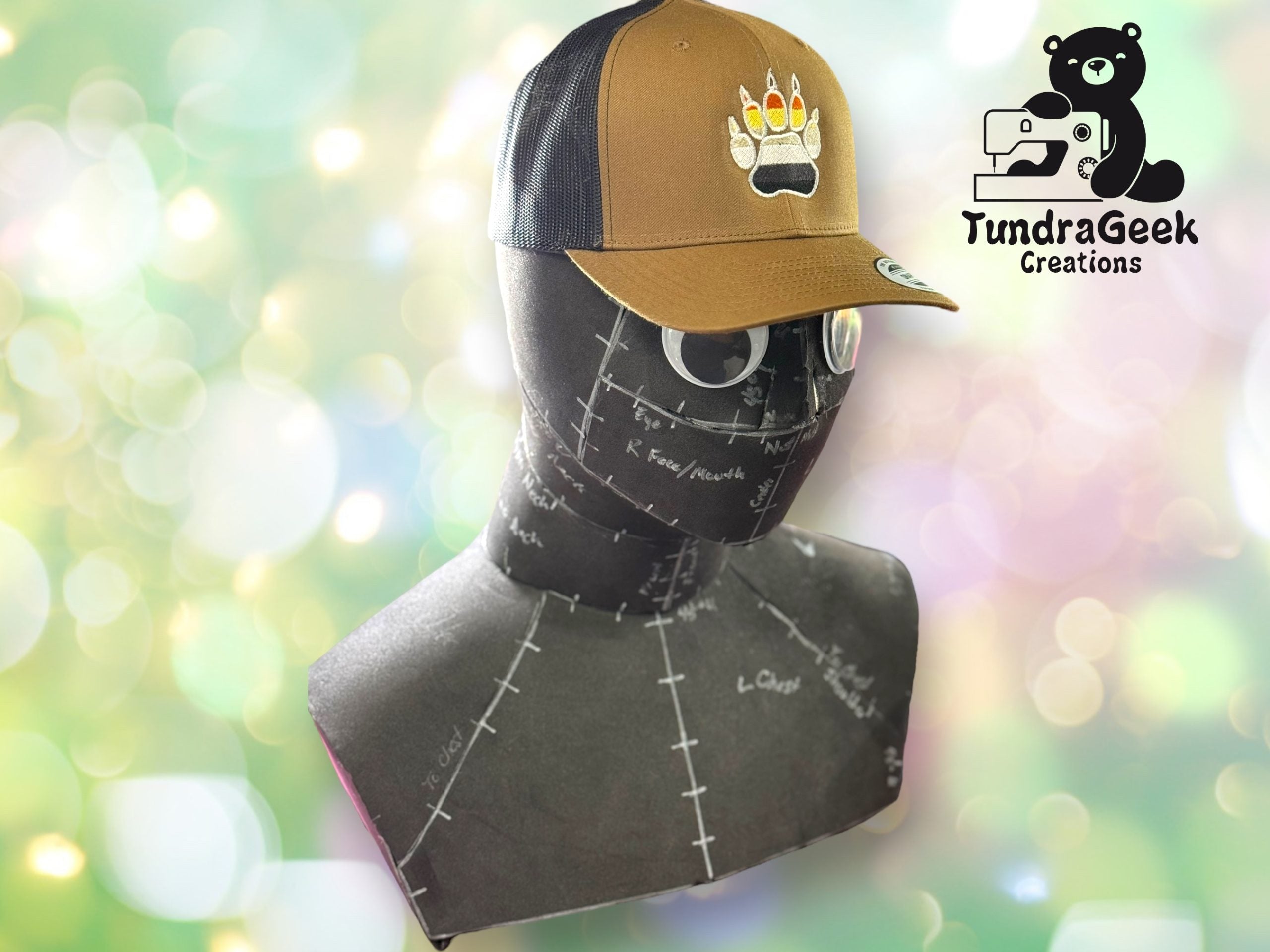 A brown and black mesh cap with a paw print logo displayed on a dress form mannequin, with the TundraGeek Creations logo in the background.