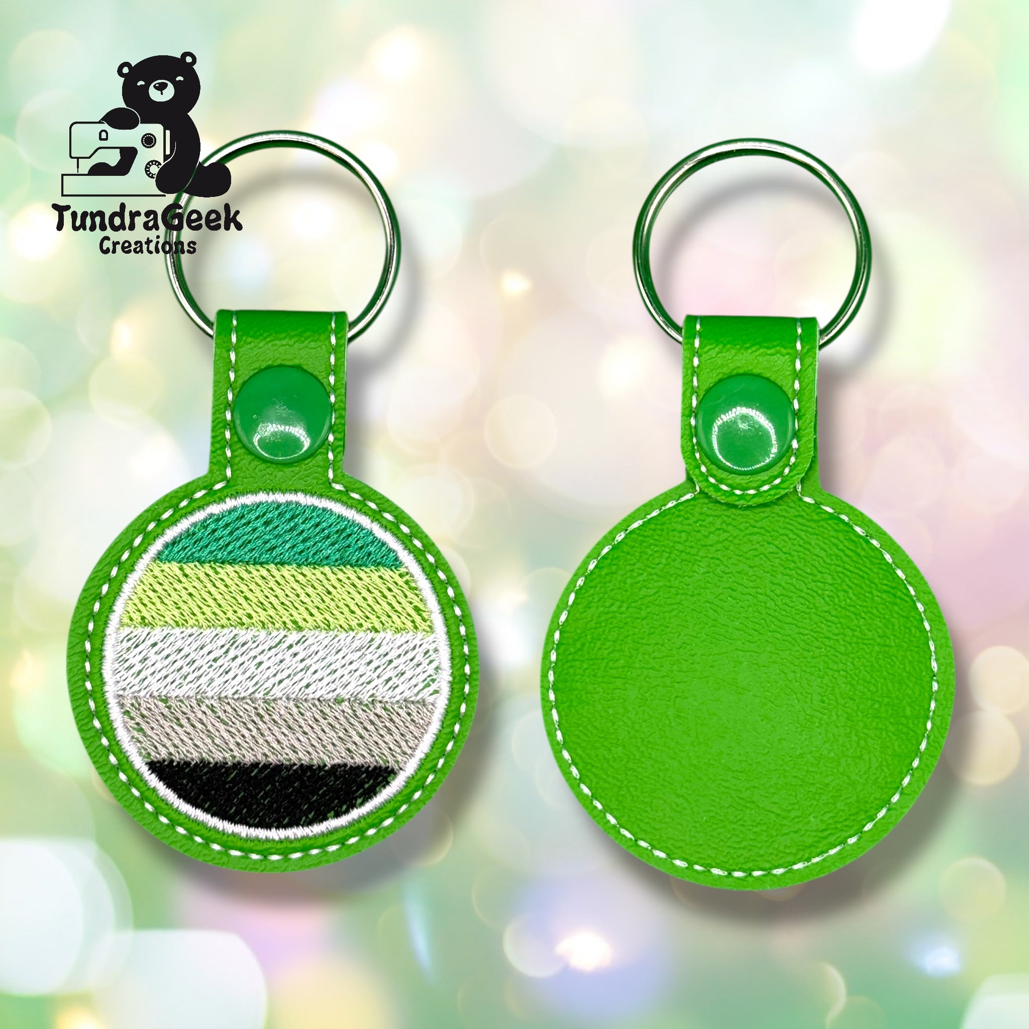 Two green round keychains are shown; one features the agender pride flag in stitched stripes, the other is plain. Both have metal rings and white stitching.