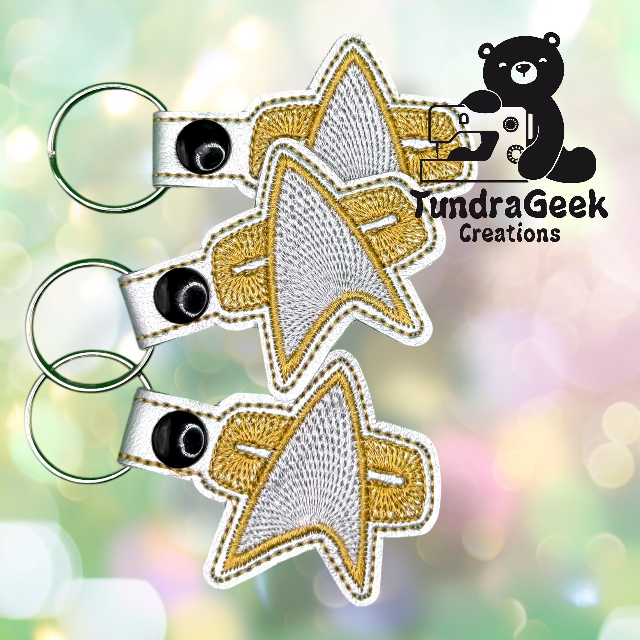 Three embroidered keychains shaped like the Star Trek insignia with gold and silver thread, displayed next to the TundraGeek Creations logo.