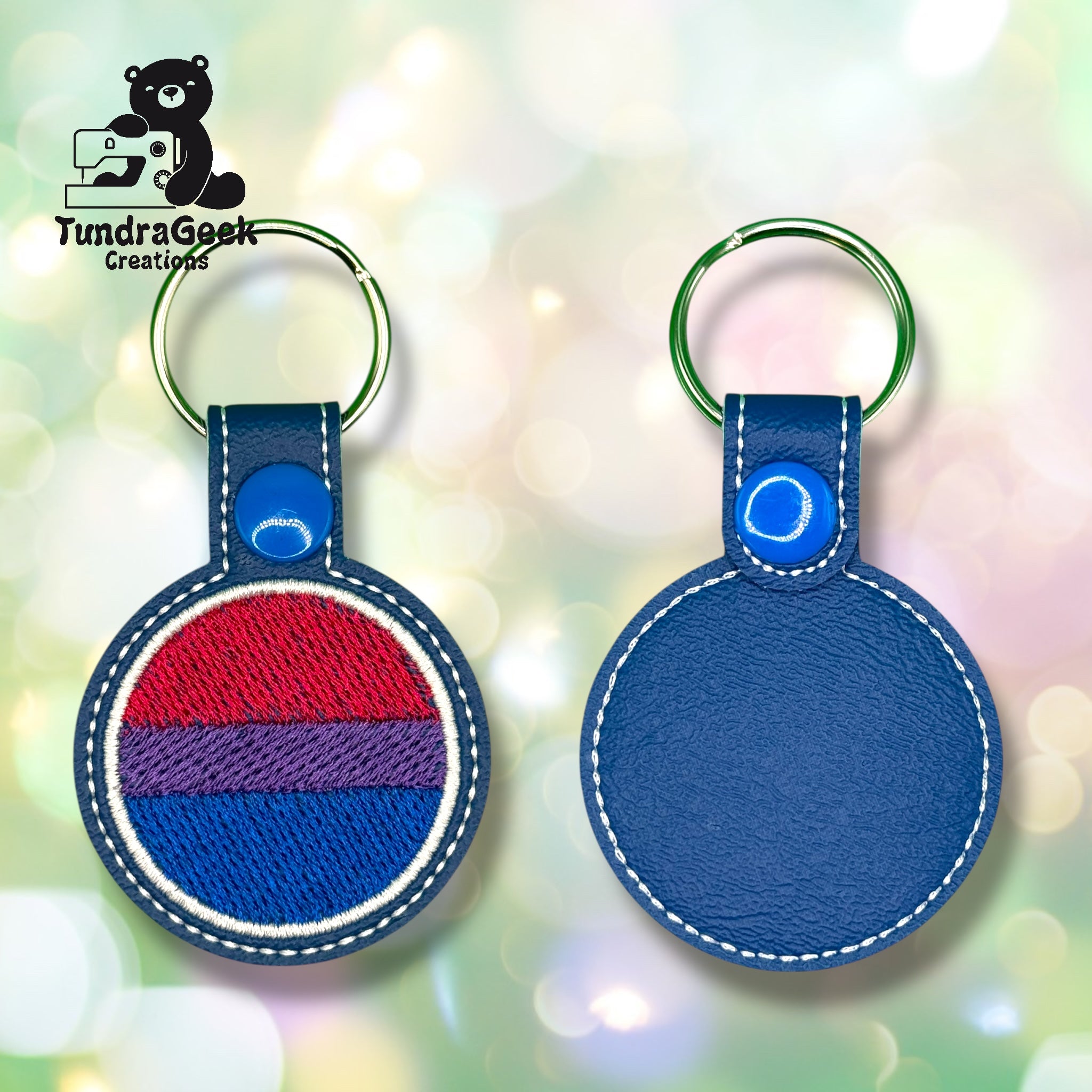 Front and back view of a round blue leather keychain with a purple, blue, and red striped embroidered patch; TundraGeek Creations logo in the top left corner.