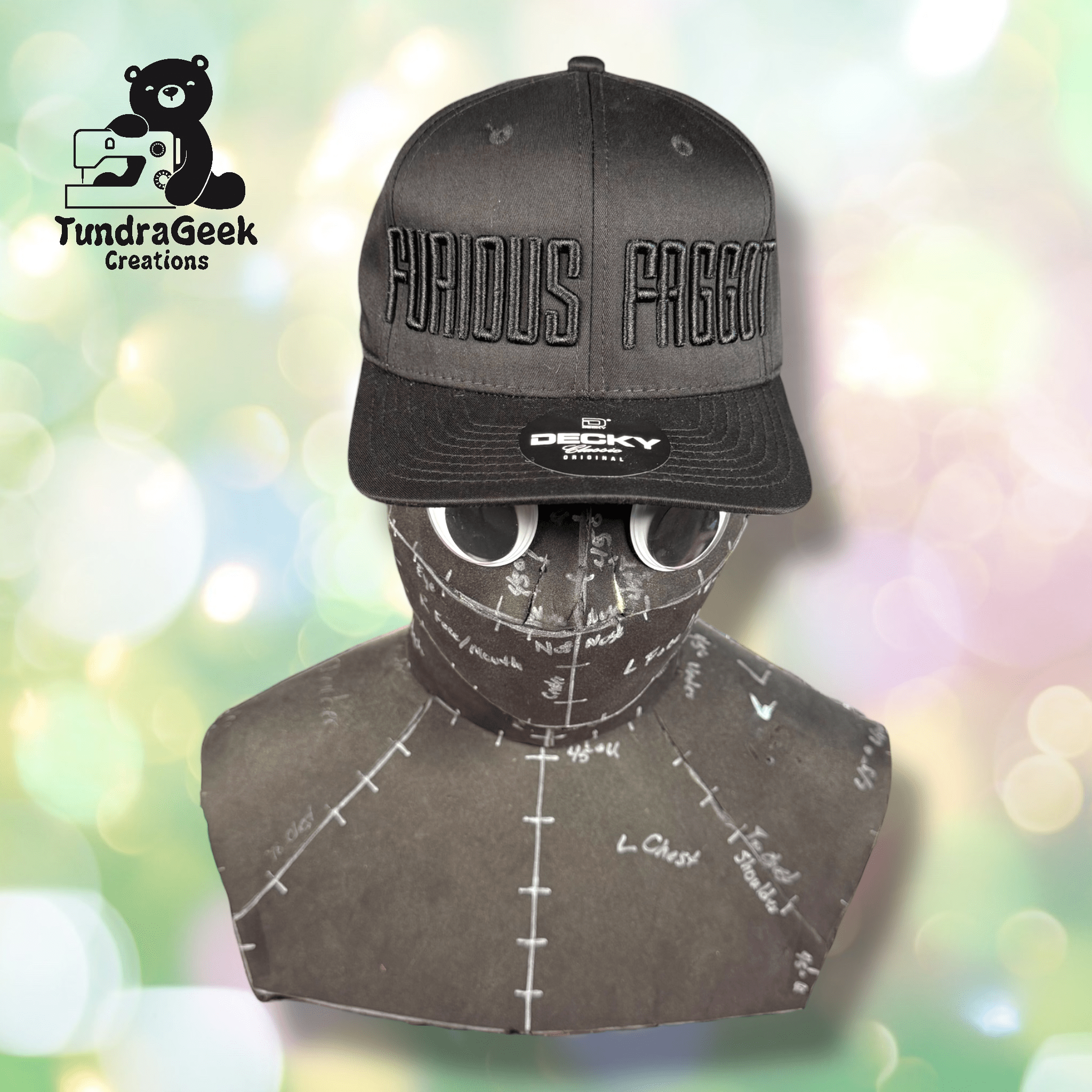 A mannequin head with a hat reading Viridis Faggot, sunglasses, and a cloth cover with white markings; TundraGeek Creations logo appears in the upper left corner.