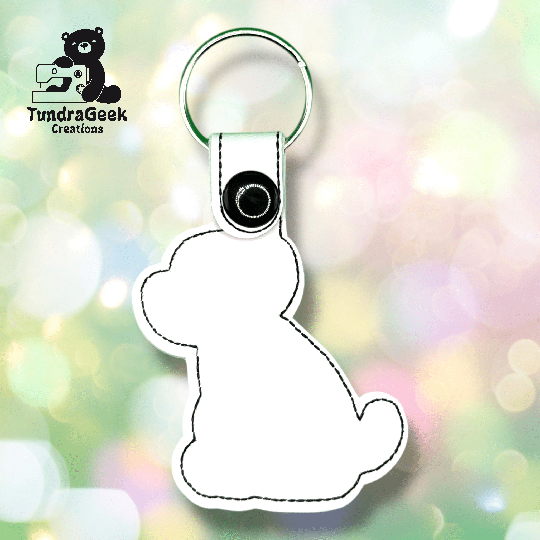 White keychain shaped like a sitting bear with black stitching and snap, attached to a metal key ring. TundraGeek Creations logo in the upper left corner.