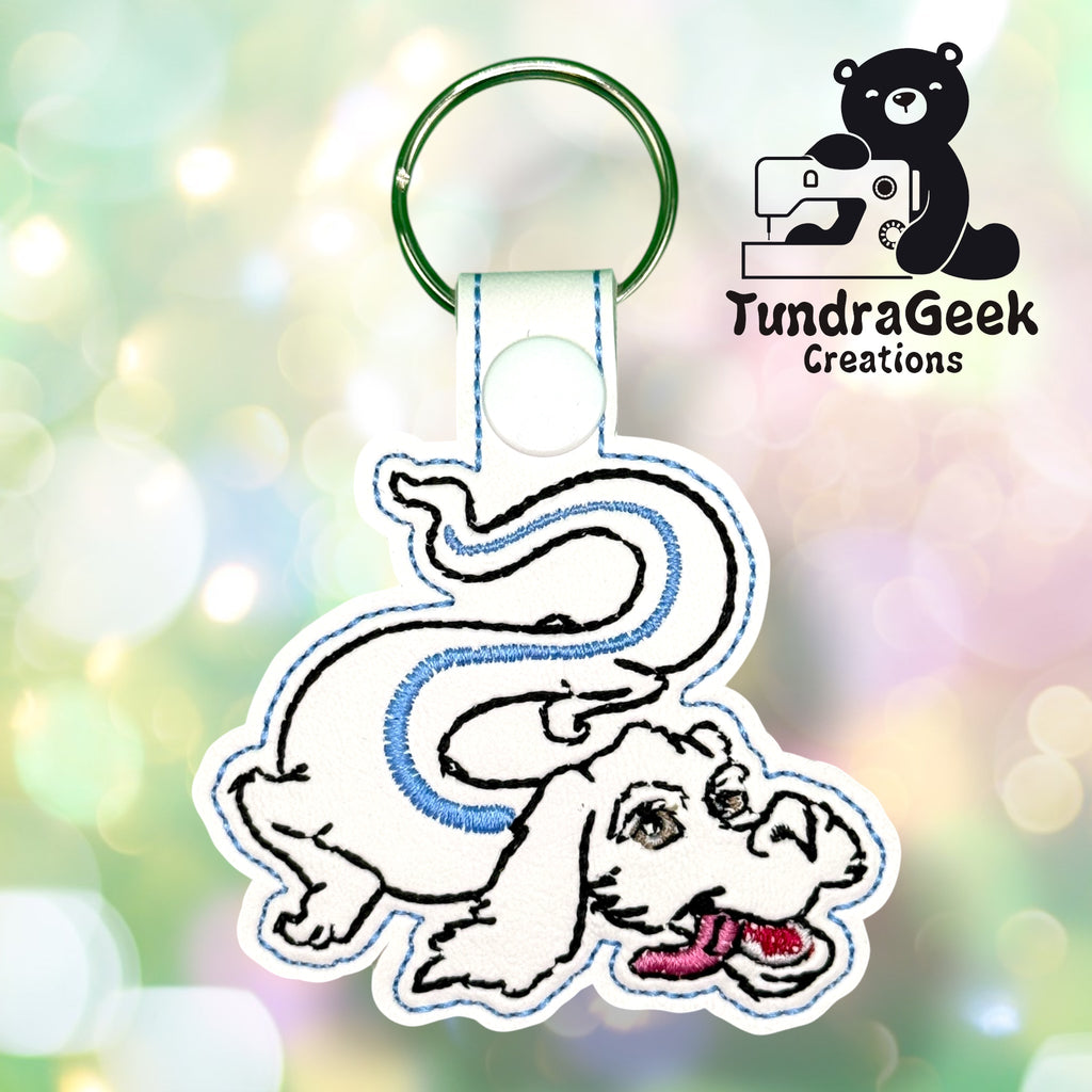 Embroidered keychain featuring a white, cartoon-style dragon with blue accents on a green key ring, shown with the TundraGeek Creations logo in the background.