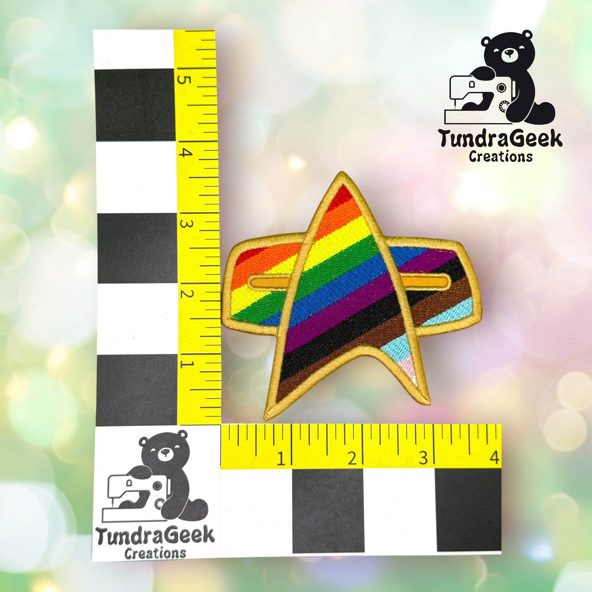A Star Trek-inspired badge with a rainbow Pride design, measuring about 3 inches across, is displayed next to a ruler grid. The logo TundraGeek Creations appears in two corners.