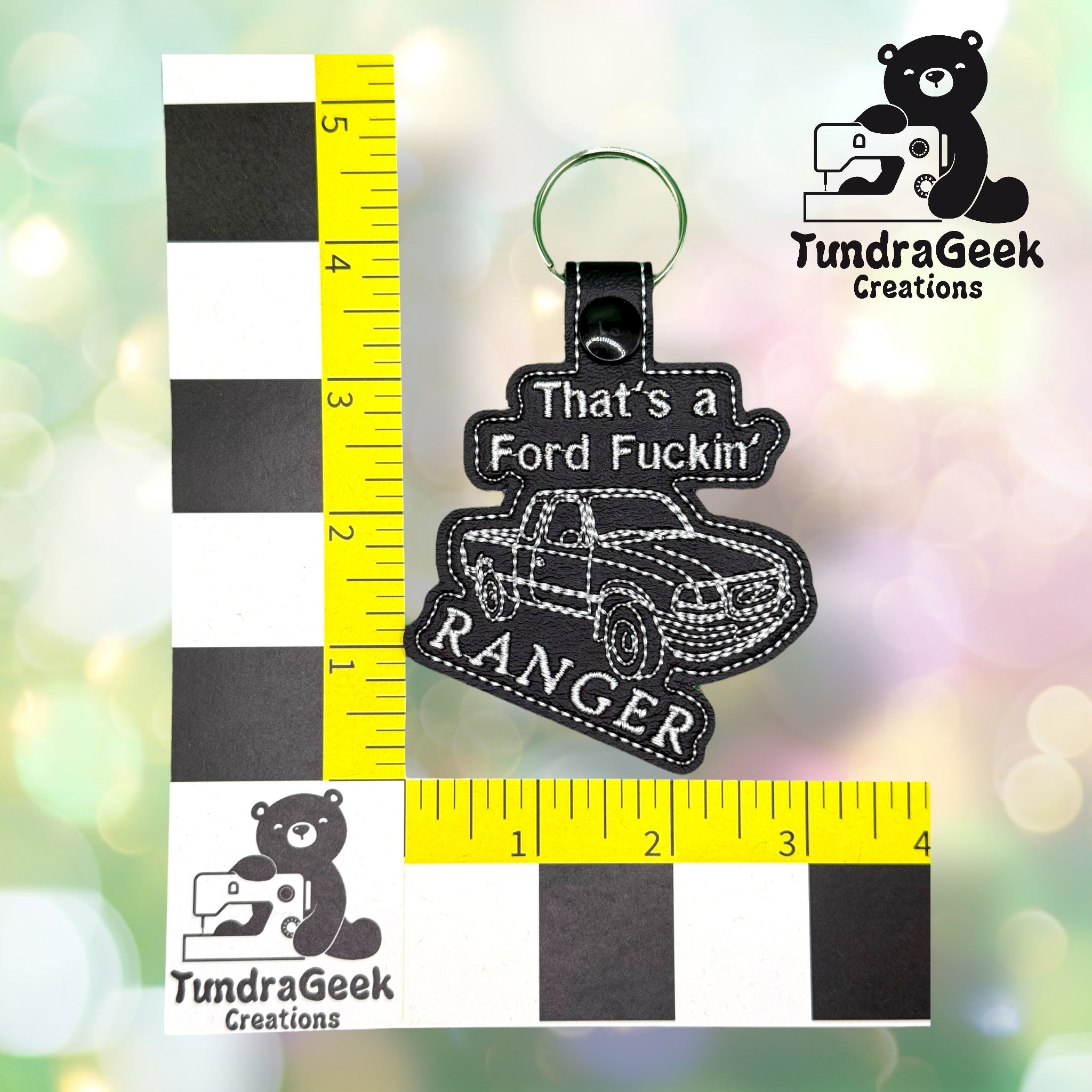 A keychain with the text Thats a Ford Fuckin Ranger and an embroidered truck, shown next to rulers for scale. TundraGeek Creations logo is visible in the background.
