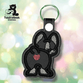 A keychain featuring a black and white embroidered bunny with a red heart on its rear, set against a blurred pastel background. TundraGeek Creations logo appears in the top left corner.