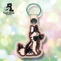 Embroidered keychain featuring a sitting dog with brown, black, and cream coloring, attached to a snap-closed loop and a green keyring. TundraGeek Creations logo in the corner.