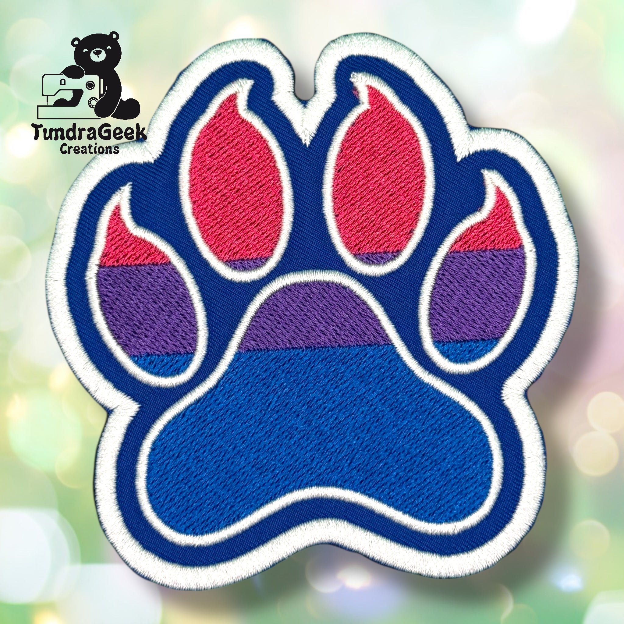 An embroidered paw-shaped patch in bisexual pride flag colors — pink/magenta, purple, and royal blue horizontal stripes. The patch has a bold blue background with white border edging, inner pad and toe details outlined in white.