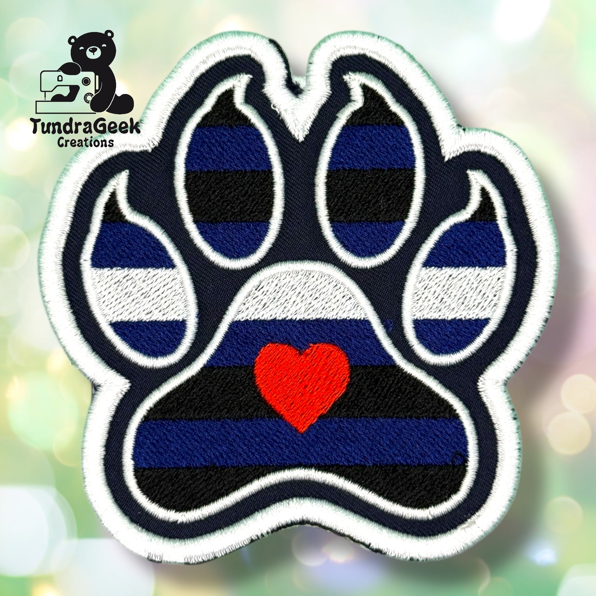 An embroidered paw-shaped patch in leather pride flag colors — alternating horizontal stripes of royal blue and black with a white stripe across the middle. A small red embroidered heart sits in the center pad area. White border edging.