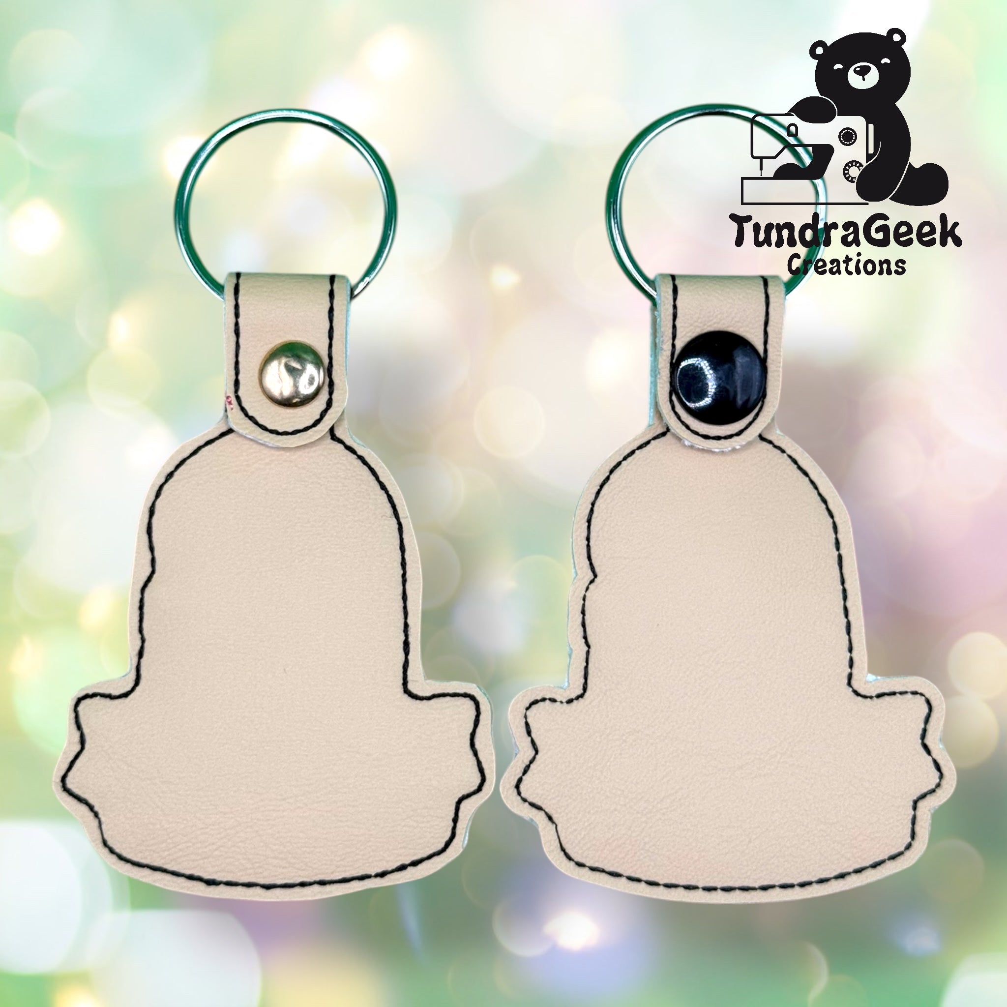 Two beige keychain holders with black stitching are displayed side by side; one shows the front with a snap button, the other shows the back. Logo TundraGeek Creations is in the top right corner.