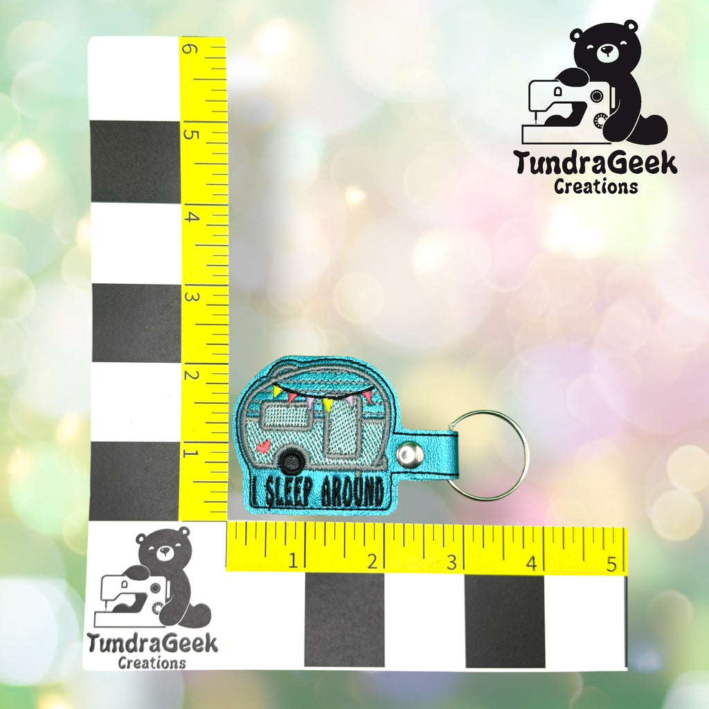 A keychain shaped like a camper with I SLEEP AROUND embroidered, placed on measured grid with TundraGeek Creations logo in two corners.