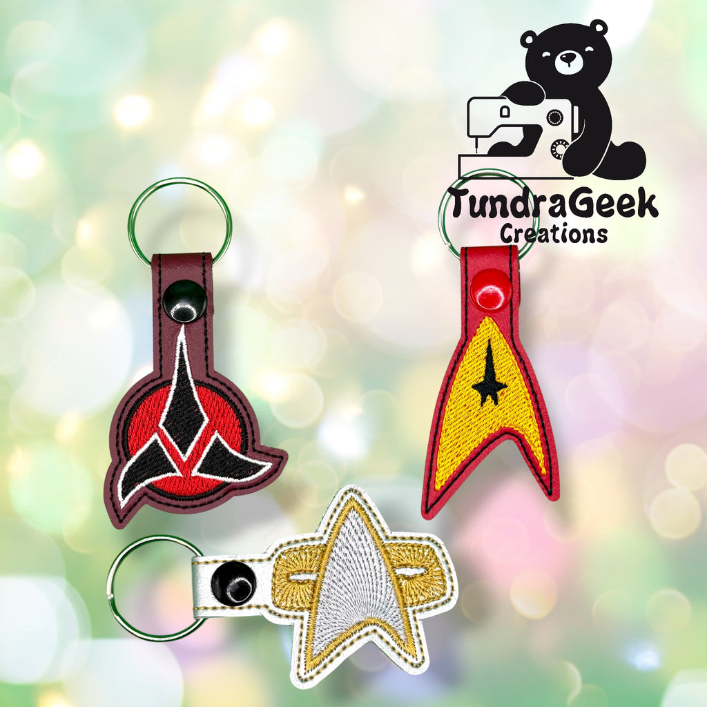 Three embroidered Star Trek-themed keychains are displayed on a blurred background, with the TundraGeek Creations logo featuring a bear with a sewing machine in the top right corner.