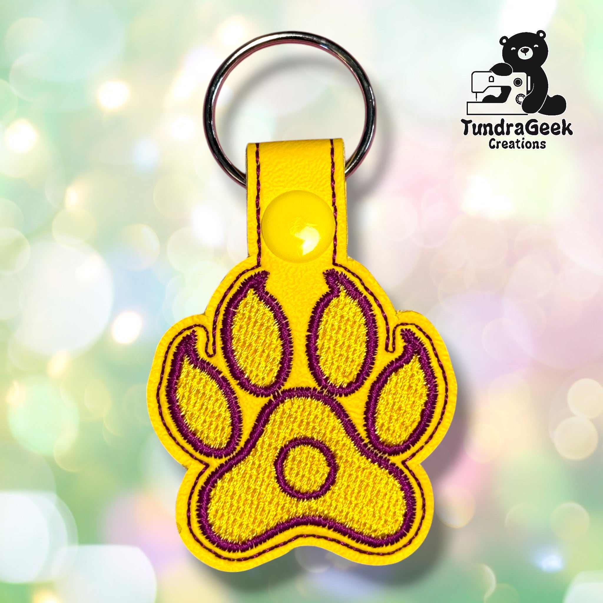 Paw-shaped keychain with the yellow and purple intersex pride flag embroidered on it