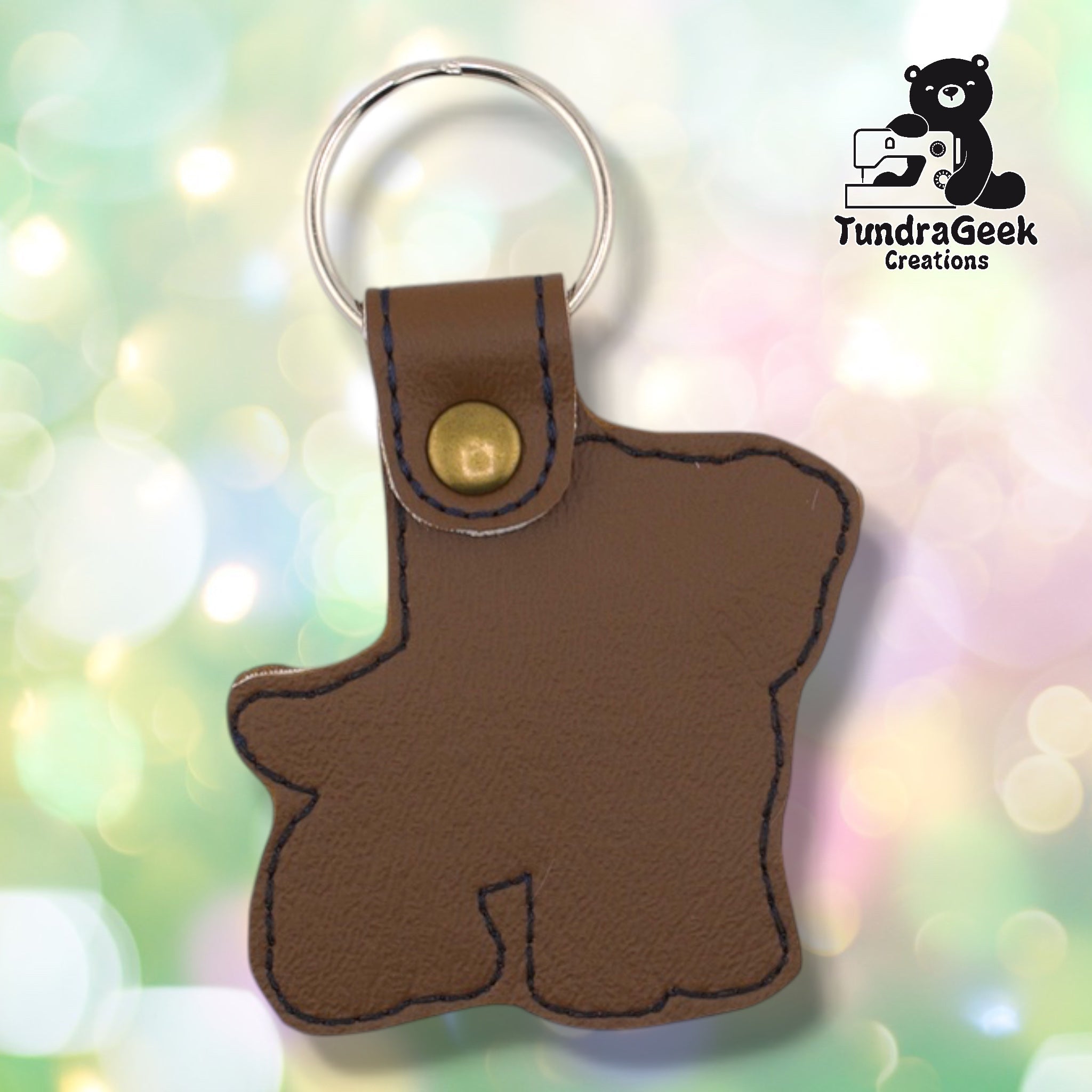 Back of a brown faux leather pibble keychain. The plain brown vinyl back panel shows dark outline stitching following the dog silhouette shape. A bronze 9mm metal rivet closure secures the tab, with a silver split ring attached above.