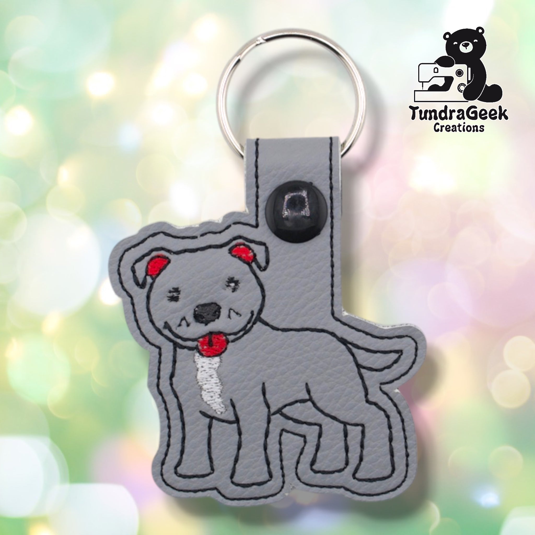 Front of a gray faux leather pibble keychain. An embroidered pit bull terrier stands facing left with a white chest blaze, red collar, red ear accents, and black nose and facial detail stitching on a matching gray vinyl base. A black 12.5mm plastic snap closure is visible on the tab, with a silver split ring above.