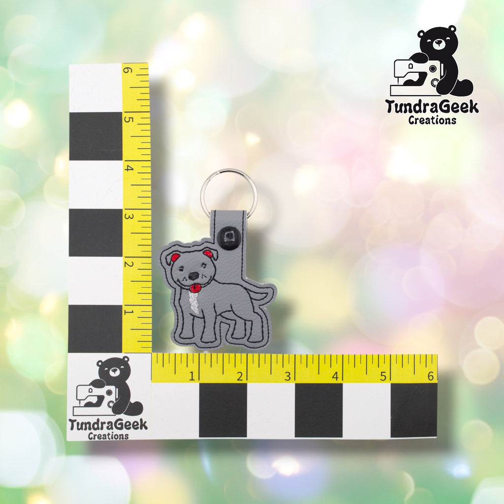Gray pibble keychain shown against a TundraGeek Creations L-shaped ruler prop. The keychain body measures approximately 2.5 inches wide by 2.25 inches tall. Total height including tab and split ring is just under 4 inches.