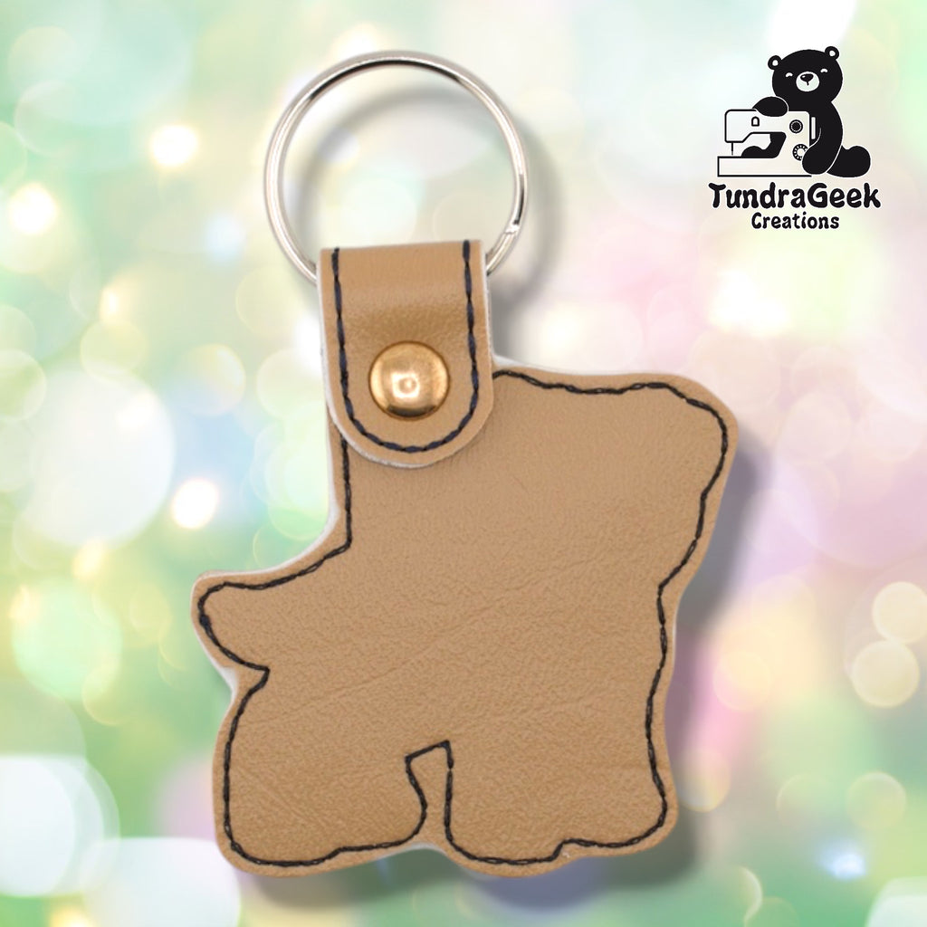 Back of a tan faux leather pibble keychain. The plain tan vinyl back panel shows dark outline stitching following the dog silhouette shape. A rose gold 9mm metal rivet closure secures the tab, with a silver split ring attached above.