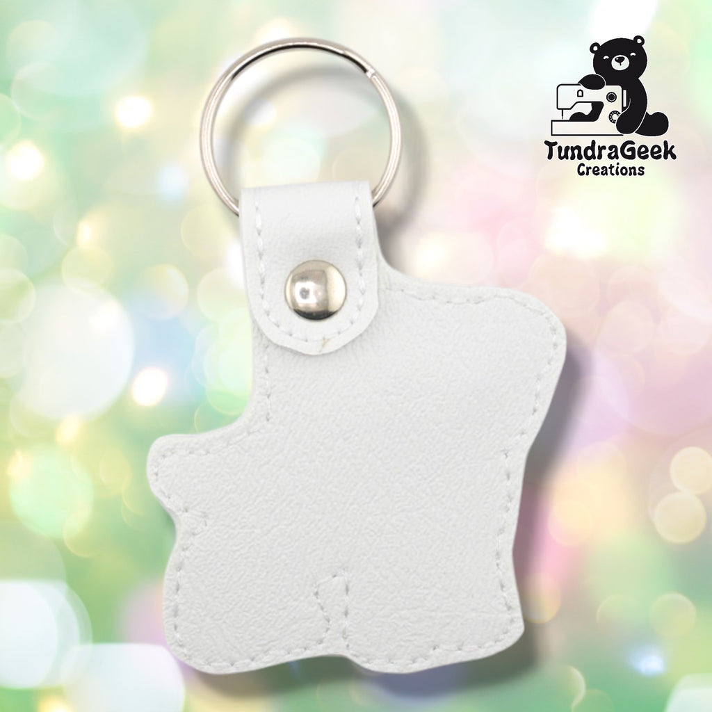 Back of a white faux leather pibble keychain. The plain white vinyl back panel shows white outline stitching following the dog silhouette shape. A silver 9mm metal rivet closure secures the tab, with a silver split ring attached above.